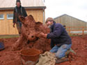 Image of: Artists making a cow from cob, a traditional Devon building technique using clay and straw.